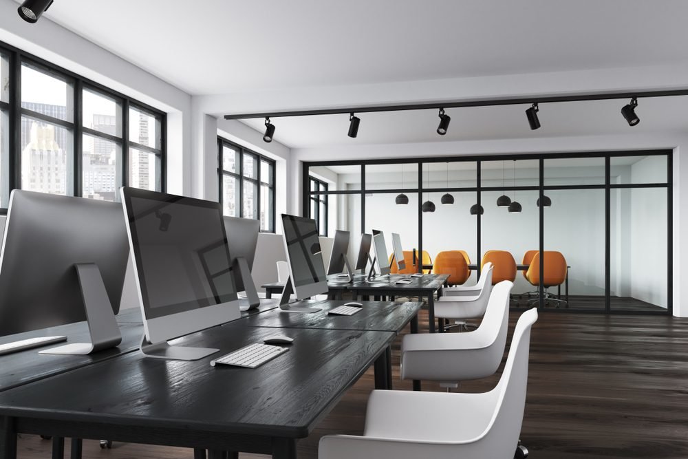 A clean modern office workspace with desks and glass conference room